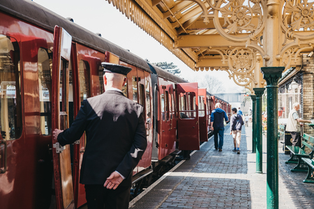 Sheringham, UK - April 21, 2019: Conductor in uniform closing a door of retro Poppy Line steam train at Sheringham station. Sheringham is an English seaside town within the county of Norfolk, UK.のeditorial素材