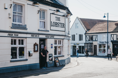 Sheringham, UK - April 21, 2019: Man stands by the entrance of The Lobster pub in Sheringham on a bright sunny day. Sheringham is an English seaside town within the county of Norfolk, UK.のeditorial素材