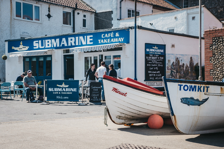 Sheringham, UK - April 21, 2019: Two fishing boats by the coast in Sheringam, people outside Submarine cafe on the background. Sheringham is an English seaside town within the county of Norfolk, UK.のeditorial素材