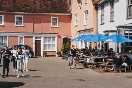 Lavenham, UK - April 19, 2019: People walking past the outdoor pub tables in Lavenham, a village in...