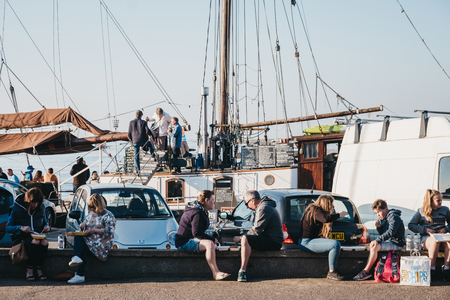 Wells-next-the-sea, UK - April 20, 2019: People sitting on a wall, eating fish and chips in Wells-next-the-sea, a seaside town and port in Norfolk, UK, famous for its beach.のeditorial素材