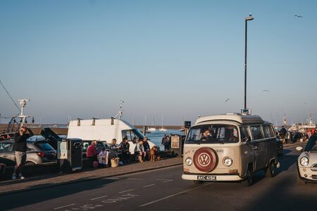 Wells-next-the-sea, UK - April 20, 2019: VW Camper van drives past people sitting on a wall, relaxing by the sea in Wells-next-the-sea, a seaside town and port in Norfolk, UK, famous for its beach.のeditorial素材