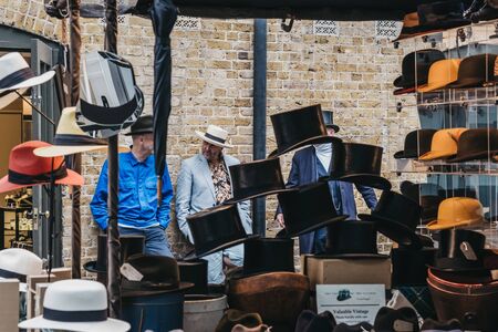 London, UK - June 15, 2019:People behind hats on sale at stall inside Spitalfields Market, one of...