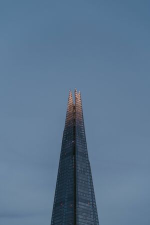 London, UK - June 22, 2019: Low angle view of top of The Shard against the sky, top illuminated,...