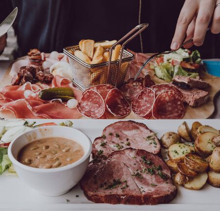 Close up of male hands holding a fork, eating cold meats platter with chips, plate with pork collar,...