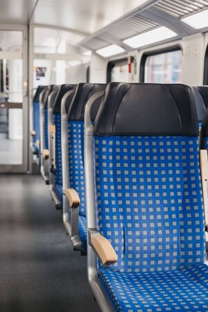 Rows of blue fabric seats with leather headrests on one side of an aisle inside empty modern train,...