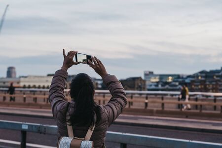 London, UK - June 22, 2019: Rear view of a woman taking pictures of the city at dusk from London Bridge, UK, selective focus. London is one of the most visited cities in the world.のeditorial素材
