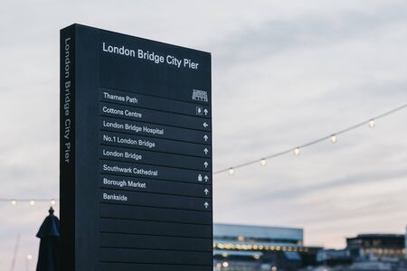 London, UK - June 22, 2019: Directional signs by London Bridge City Pier at dusk, against sky, selective focus. The pier serves as the main pier for the City of London and City Hall.のeditorial素材