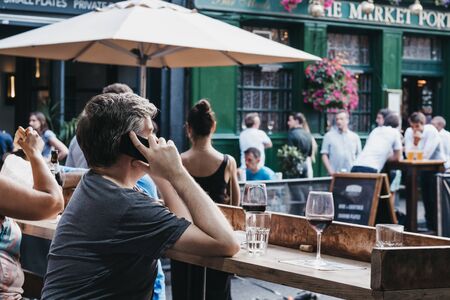 London, UK - July 23, 2019: Man talking on the mobile phone, sitting at an outdoor table of a pub inside Borough Market, one of the largest and oldest food markets in London.のeditorial素材
