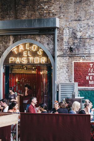 London, UK - July 23, 2019: People sitting at the outdoor tables of El Pastor Tacos restaurant in Borough Market, one of the largest and oldest food markets in London. Selective focus.のeditorial素材