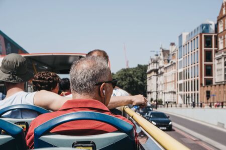 London, UK - July 29, 2019: Tourists enjoying city views from top deck of of tour bus in London on a bright summer day. Open top bus tours are amongst the most popular tourist activities in London.のeditorial素材