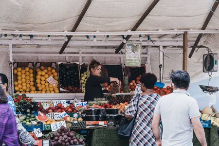 London, UK - July 16, 2019: Woman buys fresh fruits and vegetables from a market stall at Brixton Market, a community market run by local traders in the centre of Brixton, south London.のeditorial素材