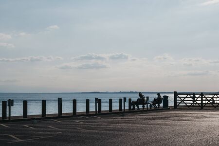 Milford on Sea, UK - July 13, 2019: People sitting on benches, reading by the sea in Milford on Sea, a traditional English village famous for breathtaking cliff top walks and great pebble beachesのeditorial素材