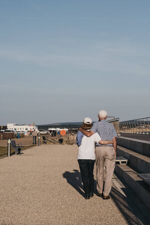 Milford on Sea, UK - July 13, 2019: Senior couple walking with arms around each other in Milford on Sea, a traditional English village famous for breathtaking cliff top walks and pebble beaches.のeditorial素材