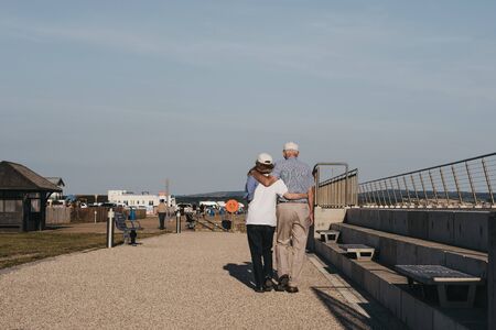 Milford on Sea, UK - July 13, 2019: Senior couple walking with arms around each other in Milford on Sea, a traditional English village famous for breathtaking cliff top walks and pebble beaches.のeditorial素材