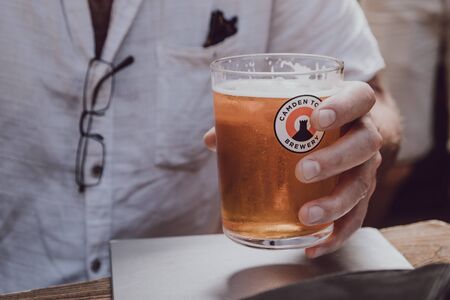 London, UK - July 29, 2019: Man holding a glass of Camden Town Brewery beer. Camden Town is a London-based brewery founded in 2010 specialising in lagers and pale ales.のeditorial素材