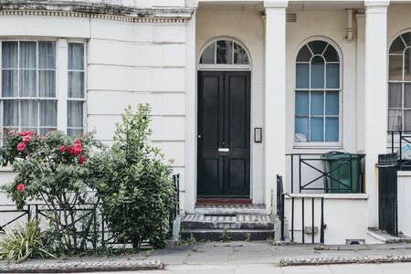 White terraced house with lower ground floor and black entrance door on a street in London, UK, in summer.の写真素材