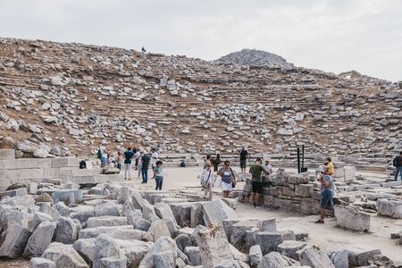 Delos, Greece - September 20, 2019: Tourists walking among ruins of ancient theatre on the Greek island of Delos, an archaeological site near Mykonos in the Aegean Sea. Selective focus.のeditorial素材