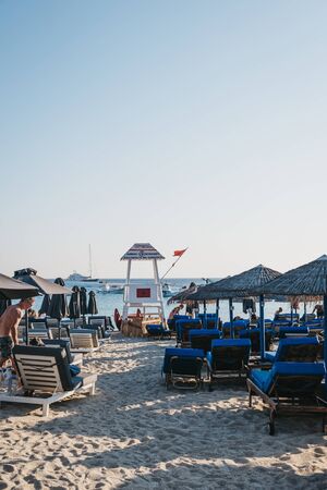Mykonos, Greece - September 19, 2019: Lifeguard tower between the rows of sunbeds in Platis Gialos beach, a popular beach on the south coast of Mykonos. Selective focus.のeditorial素材