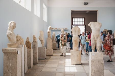 Delos, Greece - September 20, 2019: Statues inside the Archaeological Museum of Delos, a museum on the historic island of Delos in the South Aegean, Greece, people walking by, selective focus.のeditorial素材