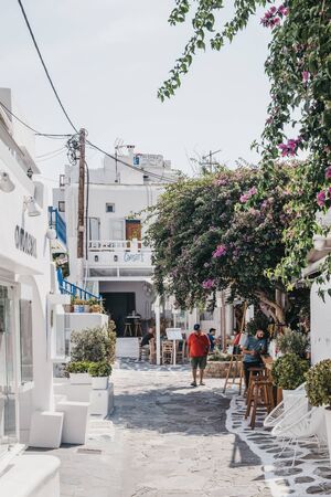 Mykonos Town, Greece - September 23, 2019: Man in red t-shirt walking past shops and restaurants on a narrow street in Hora (also known as Mykonos Town), the islands well-preserved port and capital.のeditorial素材
