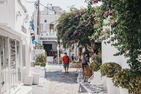 Mykonos Town, Greece - September 23, 2019: Man in red t-shirt walking past shops and restaurants on a narrow street in Hora (also known as Mykonos Town), the islands well-preserved port and capital.のeditorial素材