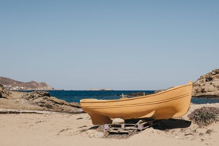 Unidentified yellow wooden boat on a beach in Mykonos, Greece, selective focus.の写真素材