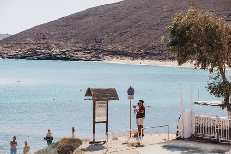 Mykonos, Greece - September 23, 2019: Two men taking photos of Panormos Beach sign. Panormos beach...