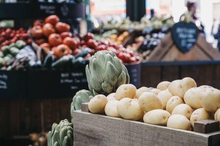 New potatoes on sale at a market stall, variety of other fruits and vegetables in crates on the background, selective focus.の写真素材
