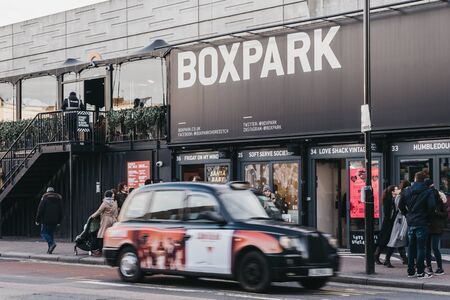 London, UK - December 29, 2019: People and taxi in front of shops at BOXPARK Shoreditch, London,...