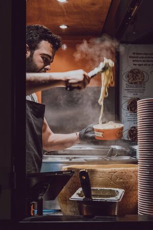 London, UK - November 26, 2019: Seller serving pasta at The Cheese Wheel stand in Camden Market, London, one of the busiest retail destinations in London. Selective focus, motion blur.のeditorial素材