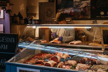London, UK - November 29, 2019: Woman cutting meat at a meat and poultry stand in Borough Market, one of the largest and oldest food markets in London.のeditorial素材