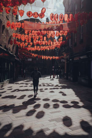 London, UK - March 06, 2020: Rear view of a man walking under red lanterns in largely empty Chinatown area in London that is famous for its eateries and events. Dramatic light.のeditorial素材