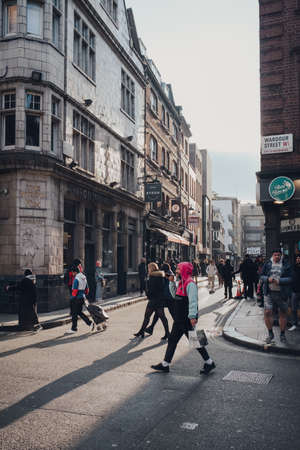 London, UK - March 06, 2020: People walking on Wardour Street in Soho, an area of London famous for LGBTQ+ bars, restaurants and clubs, at sunset.のeditorial素材