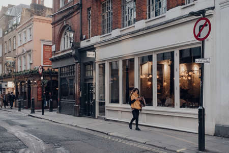 London, UK - March 06, 2020: Row of cafes and restaurants in Soho, an area of Central London famous for bars and eateries, woman walking past, motion blur.のeditorial素材
