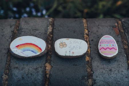 London, UK - April 12, 2020: Pebbles painted with rainbow, Easter egg and stay safe message left on the street as people support each other during lockdown because of Coronavirus.のeditorial素材