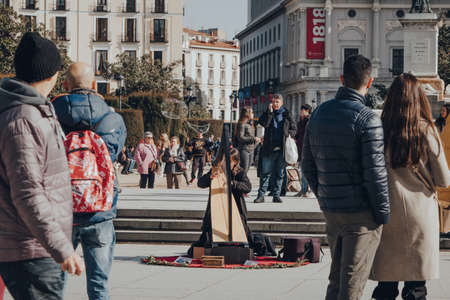 Madrid, Spain - January 26, 2020: Young man playing harp on Plaza de Oriente in Madrid, capital of Spain renowned for its rich repositories of European art, surrounded by spectators, selective focus.のeditorial素材