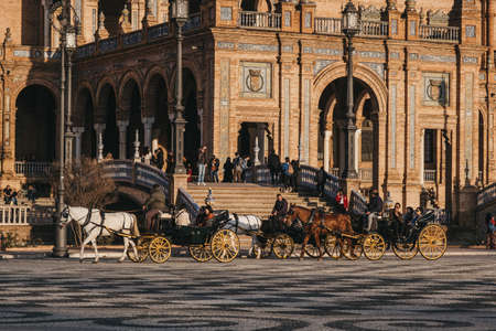 Seville, Spain - January 17, 2020: Horse-drawn carriages city tour on Plaza de EspaÃ±a, a plaza in the Parque de MarÃ­a Luisa, in Seville, Spain, built in 1928 for the Ibero-American Exposition of 1929.のeditorial素材