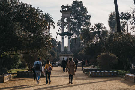 Seville, Spain - January 17, 2020: Christopher Columbus monument in Jardines de Murillo, urban park in Seville with paved walkways, benches & shade trees, people walk in front, motion blur.のeditorial素材
