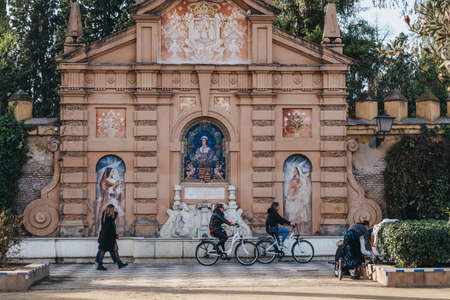 Seville, Spain - January 17, 2020: Monument to Catalina de Ribera in Jardines de Murillo, urban park in Seville with paved walkways, benches & shade trees, people and cycles moving past, motion blur.のeditorial素材