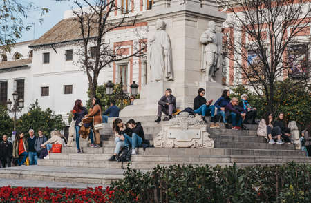 Seville, Spain - January 17, 2020:People relaxing on the stairs of the monument on Plaza del Triunfo, small plaza and popular meeting spot in Seville, Spain, known for its adjacent historic buildings.のeditorial素材