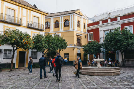 Seville, Spain - January 17, 2020: People walk on a typical street in Seville, the capital of Andalusia region in Southern Spain and a popular tourist destination, lined with orange trees.のeditorial素材