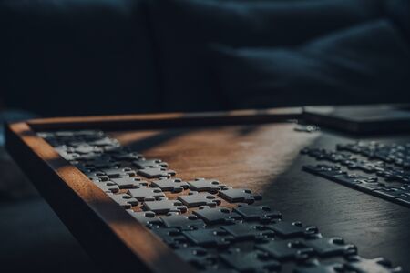 Sunlight from the window falls on the rows of white puzzle pieces on a wooden table, selective focus.の写真素材