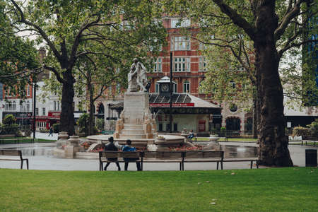 London, UK - June 13, 2020: Few people relaxing on a benches in front of a fountain in Leicester Square, one of the most popular and typically very busy tourist areas in London, UK.のeditorial素材