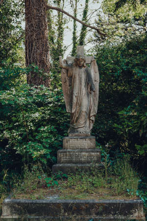 London, UK - June 16, 2020: Angel statue on a tombstone inside Hampstead Cemetery, a historic cemetery in West Hampstead, London, opened in November 1876. Against greenery, selective focus.のeditorial素材