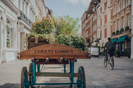 'Covent Garden" area name sign on a wooden cart with flowers on a street in Covent Garden, London, UK, on a bright summer day. Selective focus.の写真素材