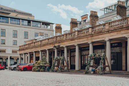 London, UK - June 13, 2020: Few people relaxing on flower decorated benches in empty Covent Garden Market, typically one of the most popular tourist sites in London, UK, on a sunny summer day.のeditorial素材