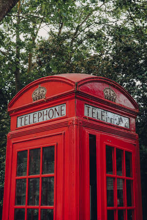 London, UK - June 20, 2020: Low angle view of red phone box against trees. Red phone boxes can be found in current or former British colonies around the world.のeditorial素材