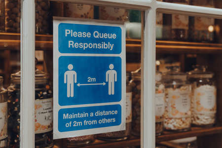 Broadway, UK - July 07, 2020: Please Queue Responsibly social distancing sign a window of a shop in Broadway, a large historic village within the Cotswolds in the county of Worcestershire, England.のeditorial素材