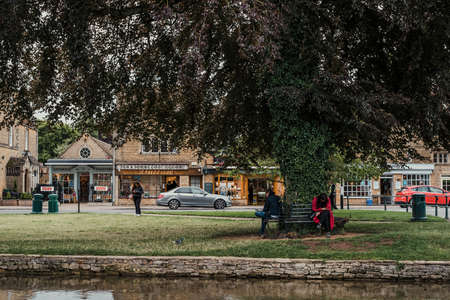 Bourton-on-the-Water, UK - July 12 2020: People taking a break, sitting under a tree by River...